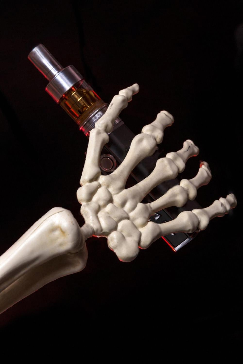 Skeleton hand holding a vape device on a black background, symbolising vape safety risks